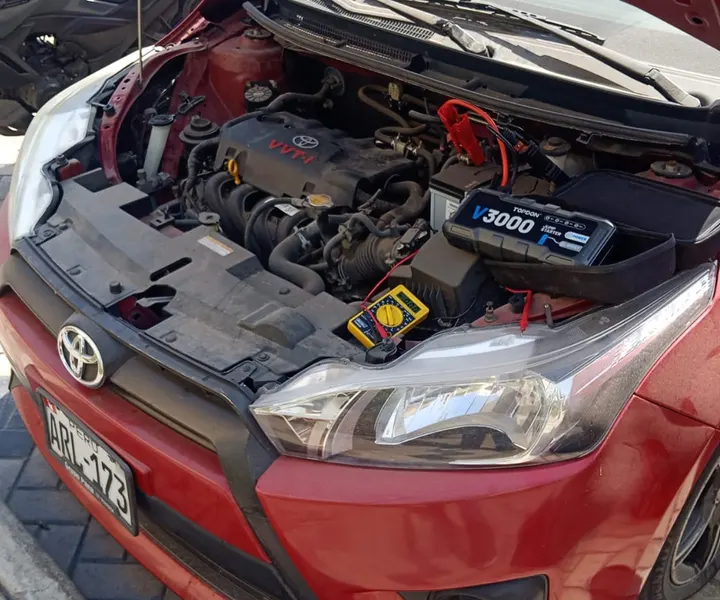 Arrancador conectado al motor de un auto rojo con moto de apoyo