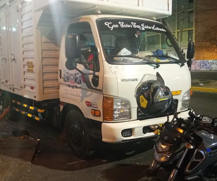 Mecánico cambiando la llanta trasera de un camión de noche junto a la moto