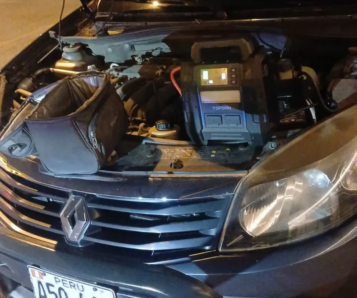 Arrancador portátil colocado en el compartimiento del motor de un auto con el capó abierto.