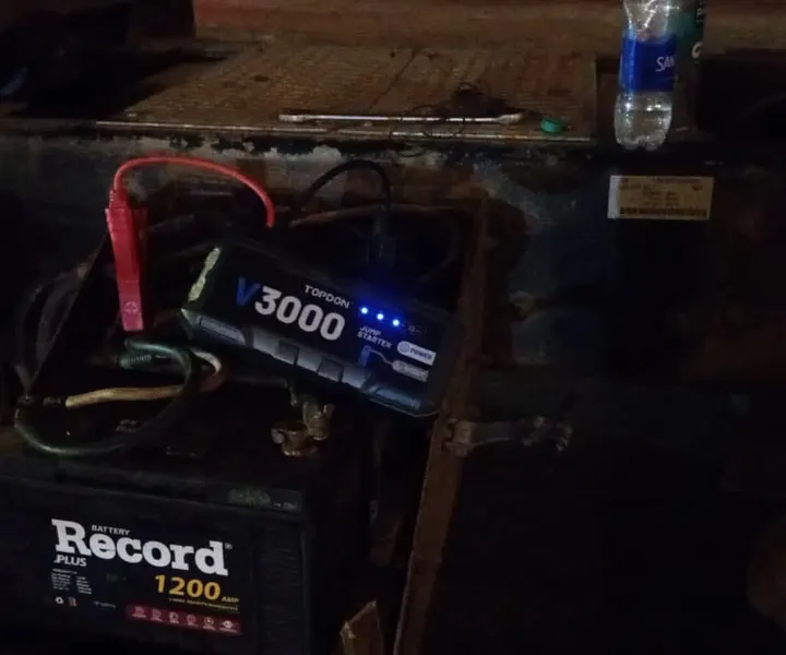 Arrancador portátil con pinzas conectado a la batería de un vehículo durante la noche.