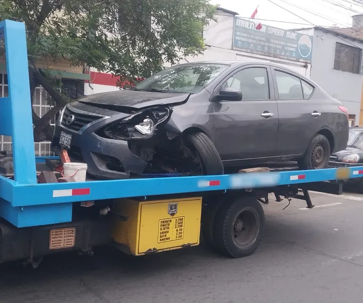 Sedán oscuro con el frente dañado cargado en una grúa de plataforma.